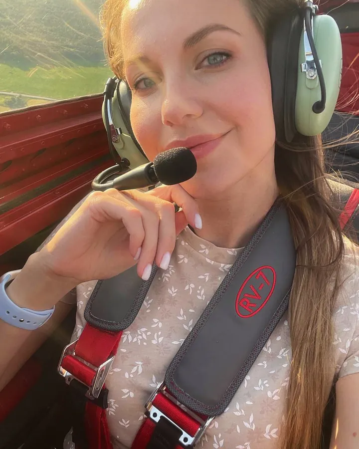 Ксения в кабине легкого самолета RV-7 в полете: авиагарнитура с микрофоном, ремни, внизу земля