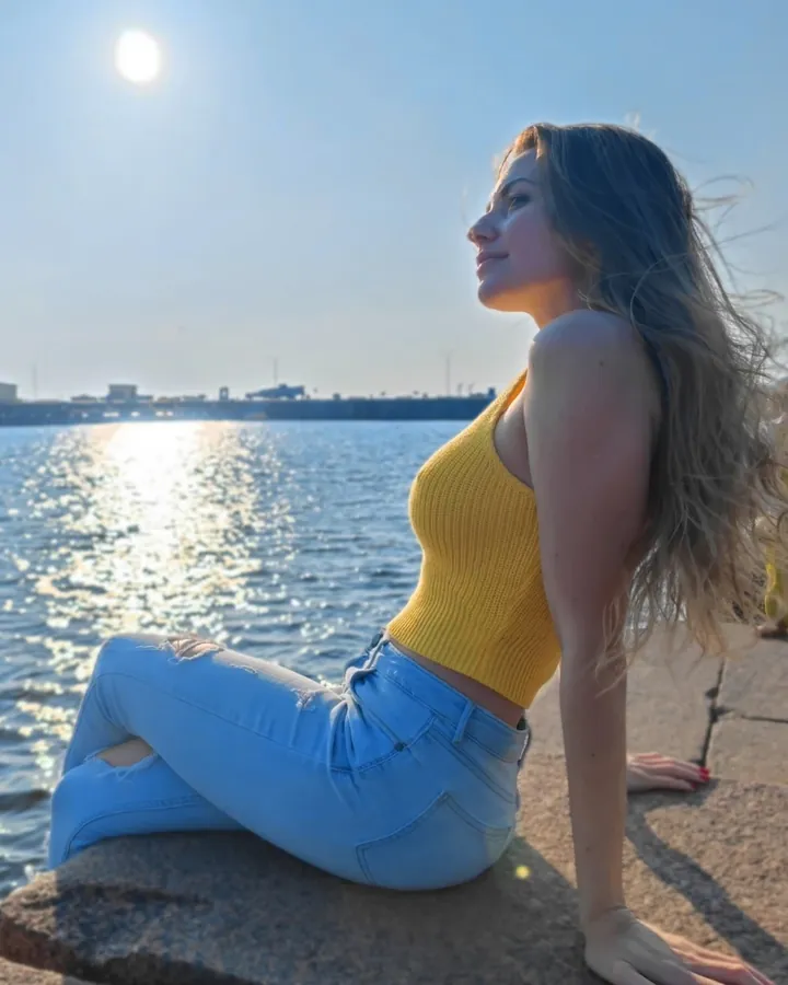 Ксения сидит на гранитной набережной у залива, над водой солнце